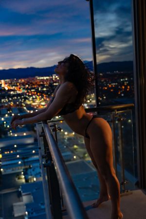 Boudoir image of female silhouette overlooking Las Vegas city lights from a high-rise balcony at dusk with colorful clouds in the sky.