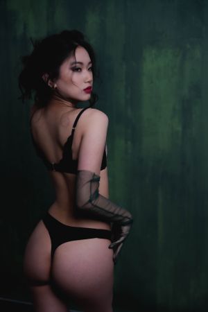 Artistic boudoir photo featuring a woman in  dark lingerie against moody green background with dramatic lighting.