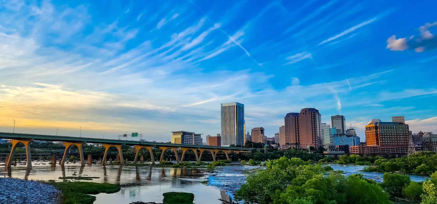 Richmond Virginia city skyline with bridge spanning the James River under vibrant blue sky.