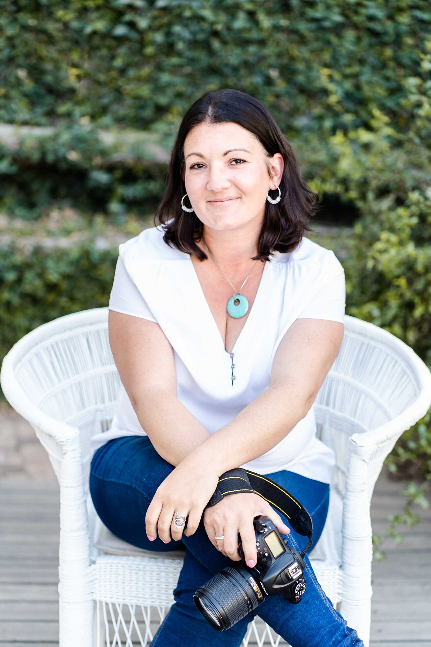 A casual portrait on a white wicker chair featuring denim jeans and a professional camera.
