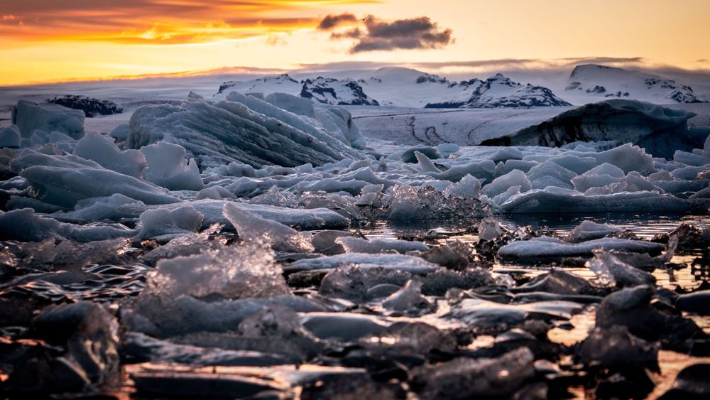 Dramatic sunset illuminates jagged ice formations on a frozen glacial landscape.
