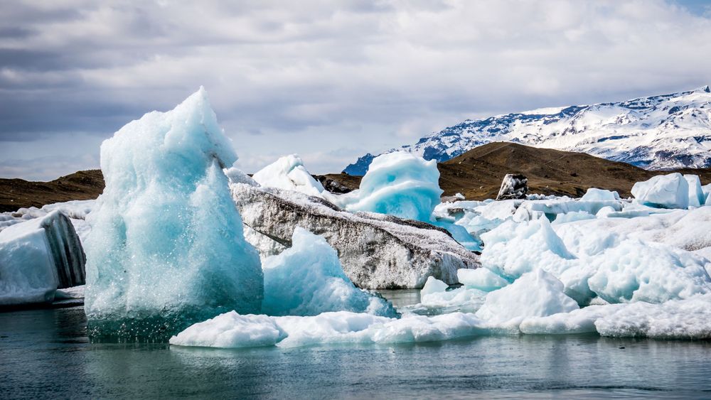 Turquoise icebergs floating in a glacial lagoon against a cloudy mountain backdrop.