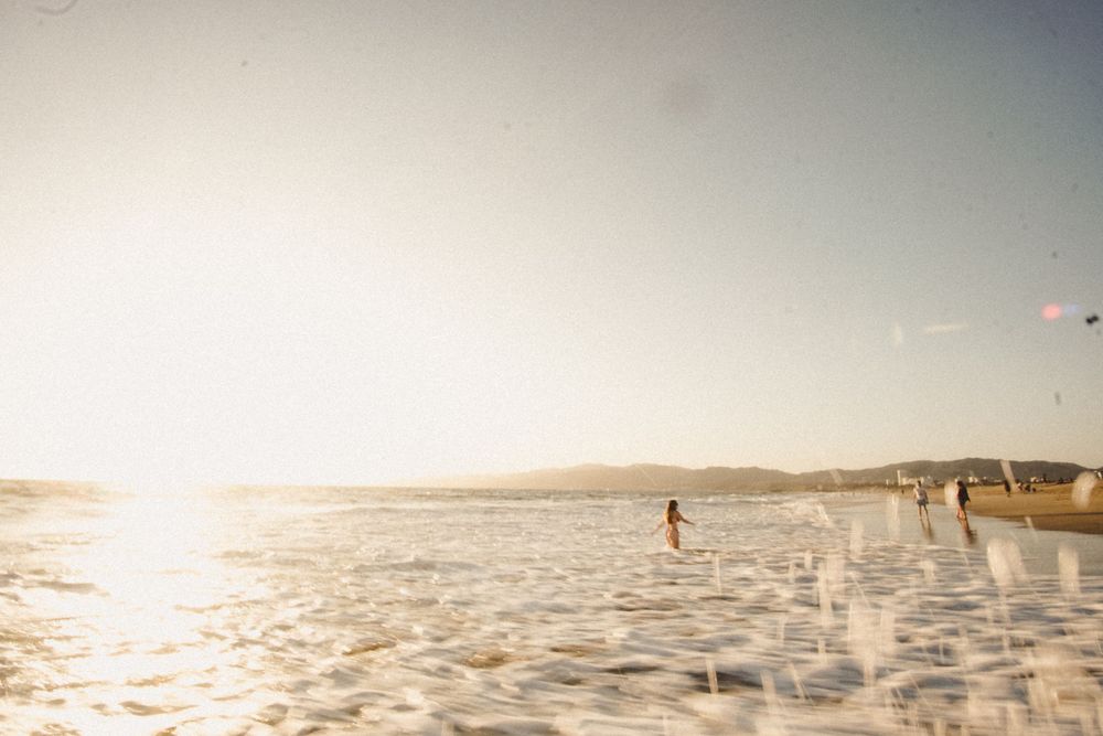People enjoy a sun-drenched beach with glittering water at sunset.