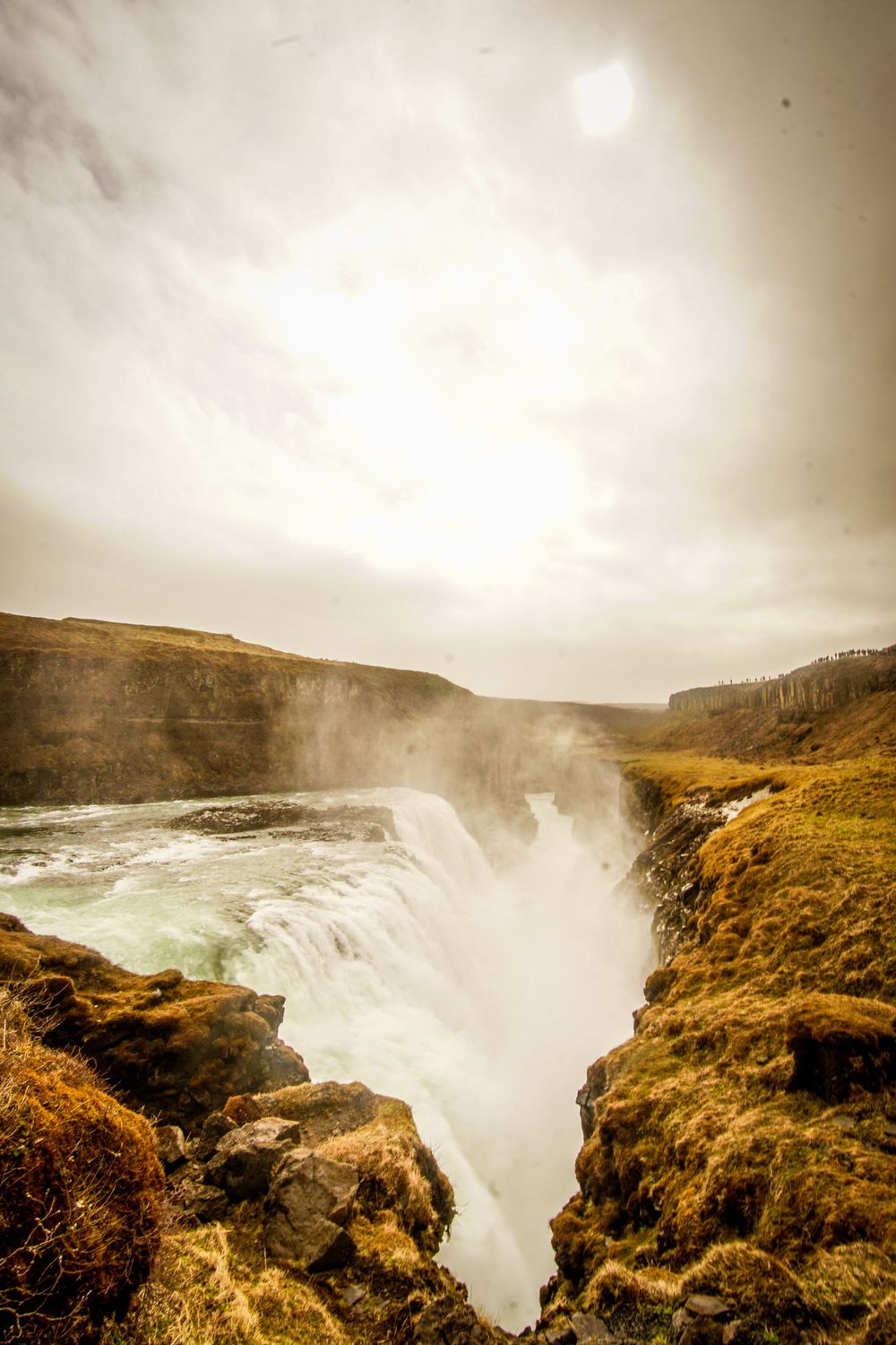 Powerful waterfall cascading through rocky canyon under misty golden sky.