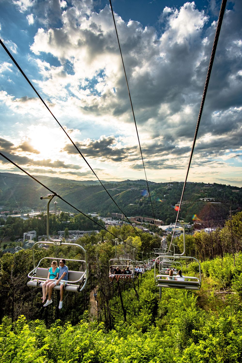 Ski lift chairs ascending mountain against dramatic cloudy sky during sunset.