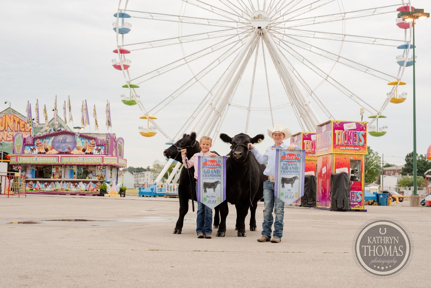 People leading show animals stand in front of a ferris wheel at a state fair.