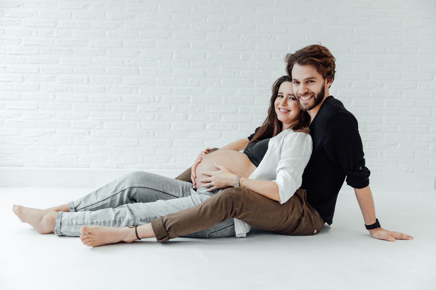 Expecting couple in casual wear posing together on white background.