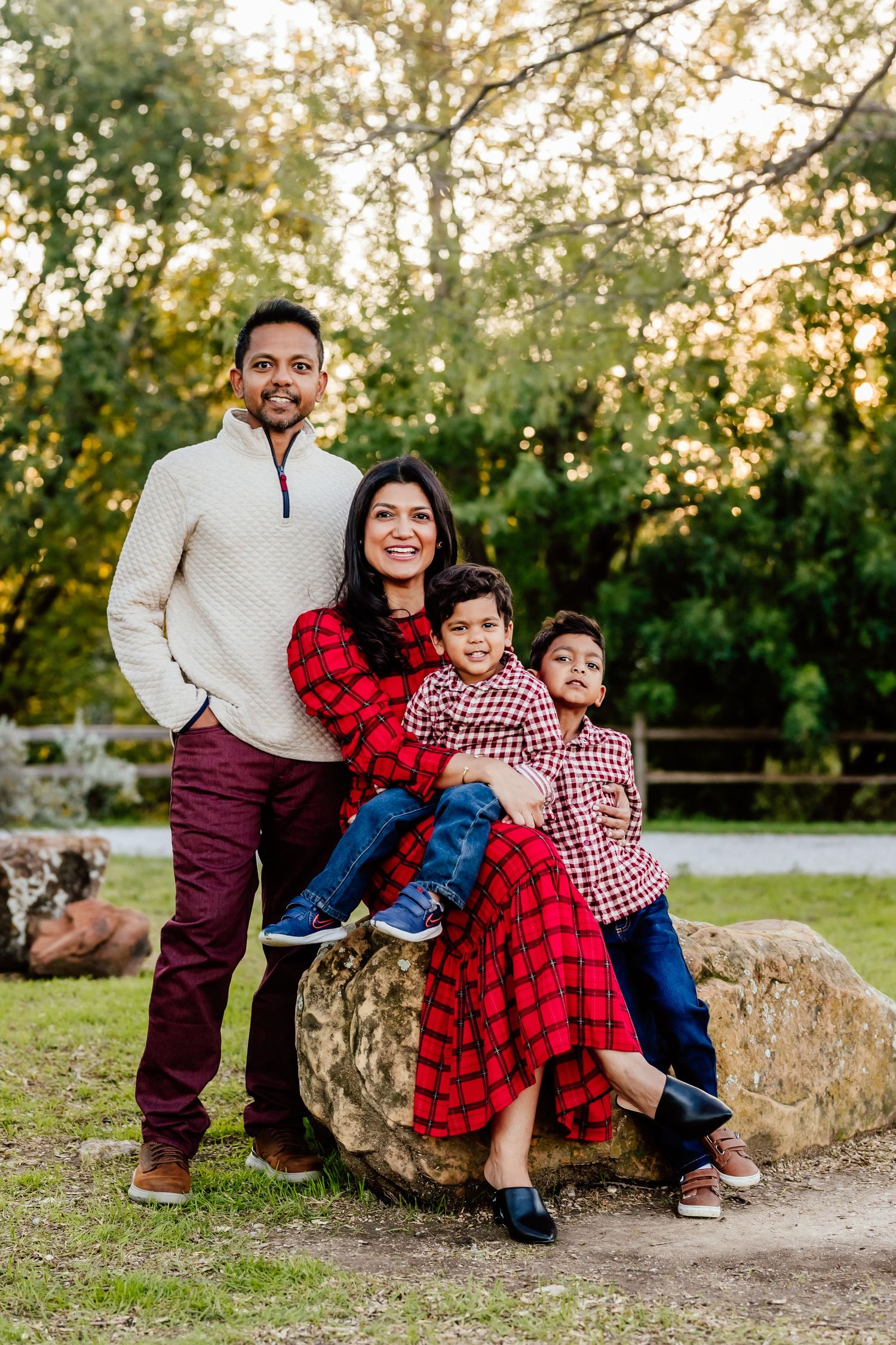 Family of four in coordinated red and white outfits pose on rock in park setting.