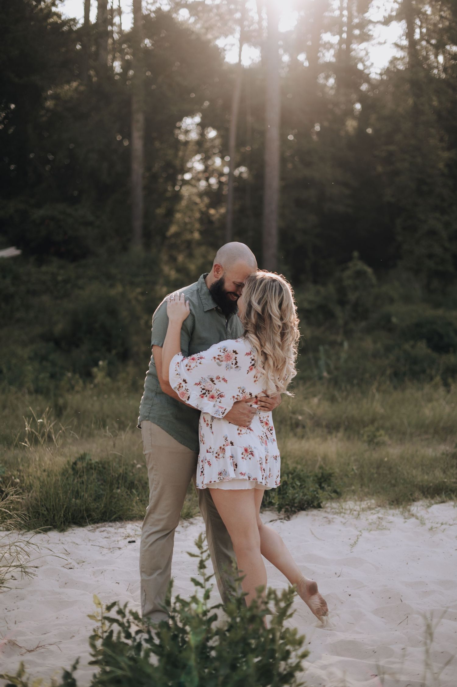 Romantic couple embracing on sandy ground with sunlit forest backdrop.