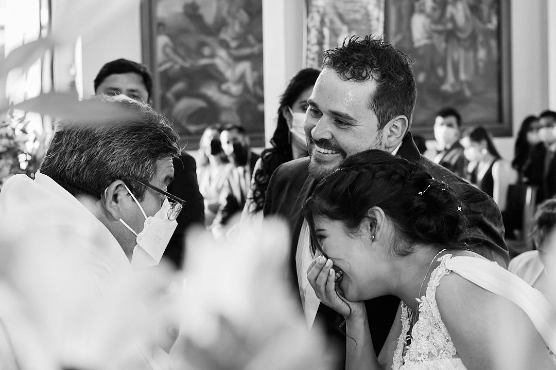 Black and white candid photograph capturing joyful laughter during a wedding ceremony.
