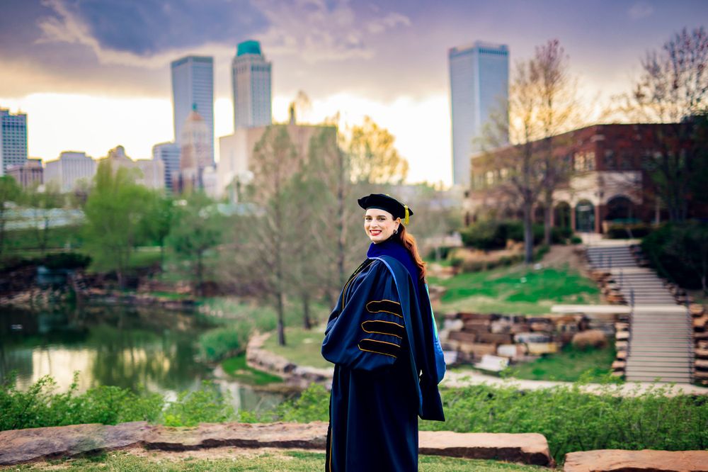 PhD graduate student with Tulsa Skyline in photo session at Centennial Park in the spring
