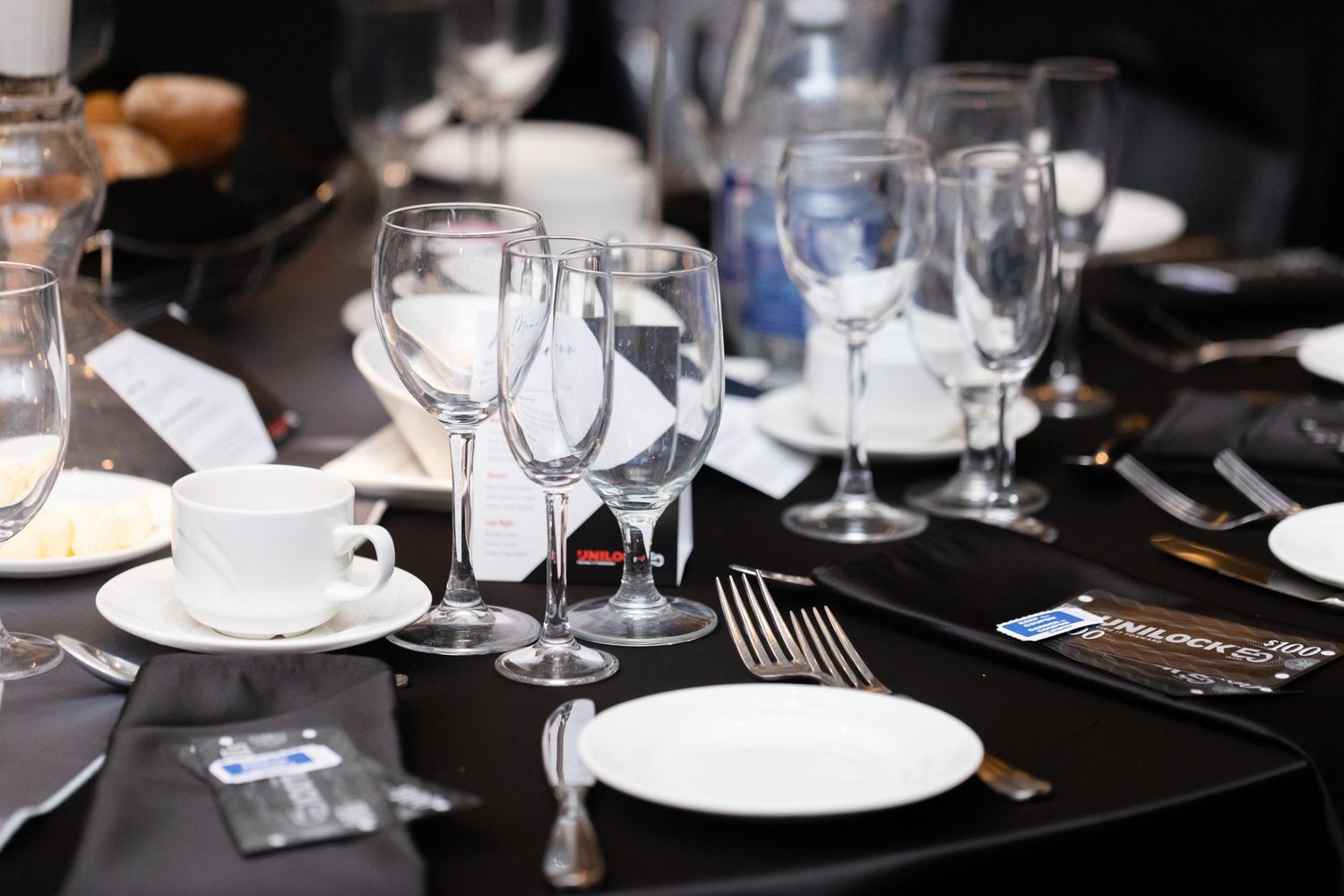 Formal table setting with wine glasses and white plates against dark background.