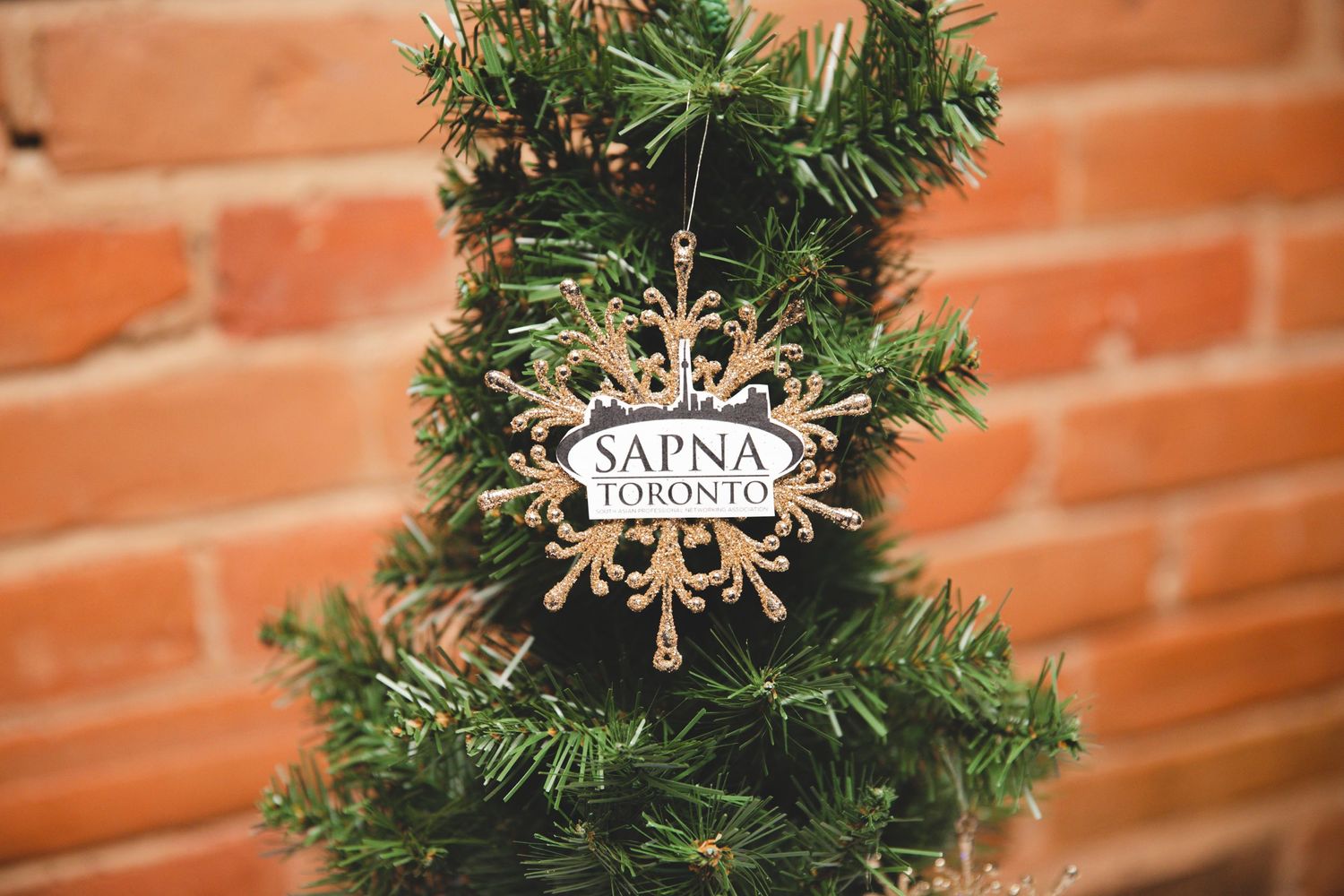 Close-up of a Christmas wreath with ornaments and holiday decor hanging against a brick wall.