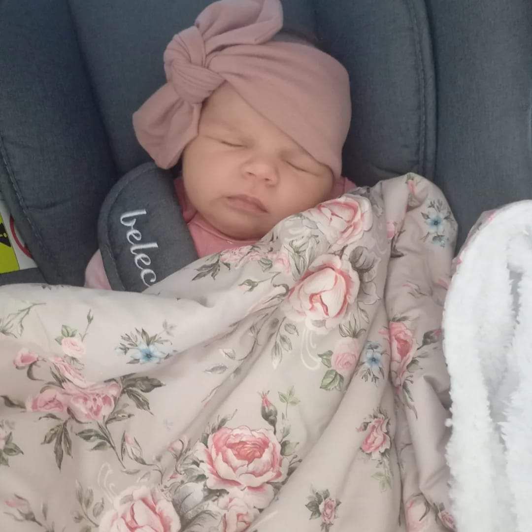 Baby sleeping peacefully in floral outfit with pink bow headband.