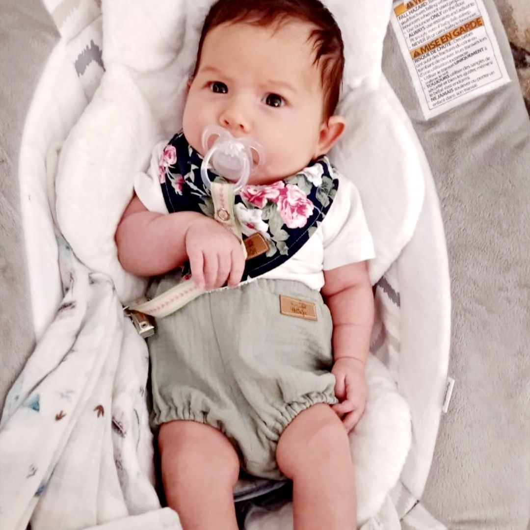 Baby in white and gray clothing rests on soft white blanket.