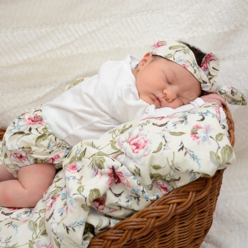 Baby sleeping in wicker basket with floral clothing and white bedding.