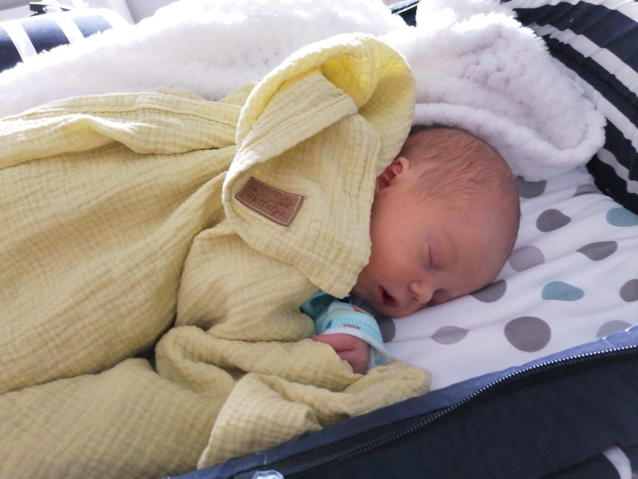 Newborn baby sleeping in yellow outfit with polka dot bedding.