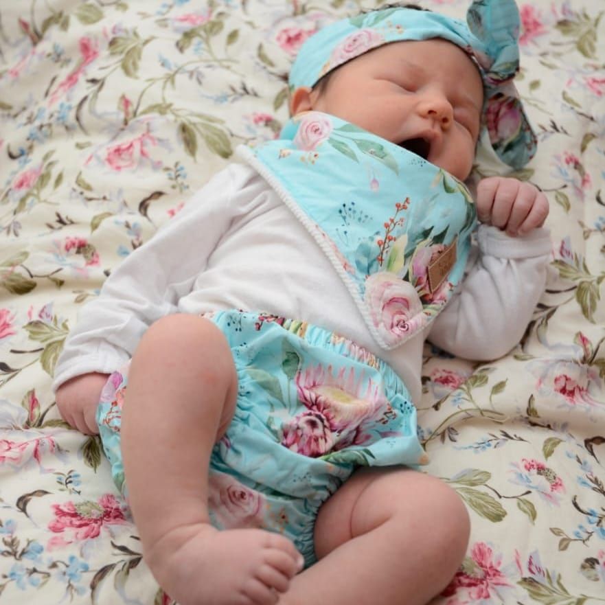 Baby in turquoise bib sleeping peacefully on floral print fabric.