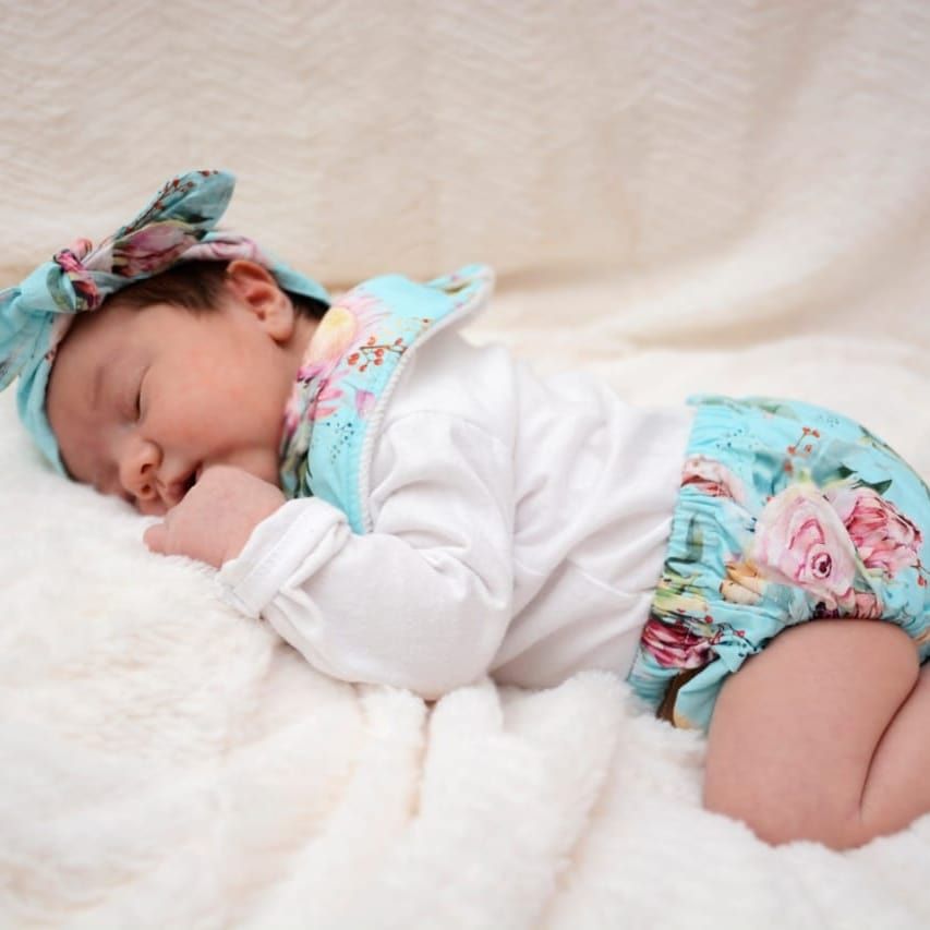 Baby resting on white bedding wearing floral turquoise outfit.