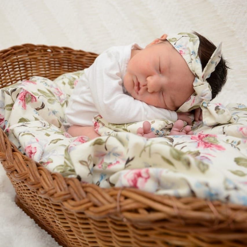Peaceful newborn sleeping in woven basket with floral blanket.