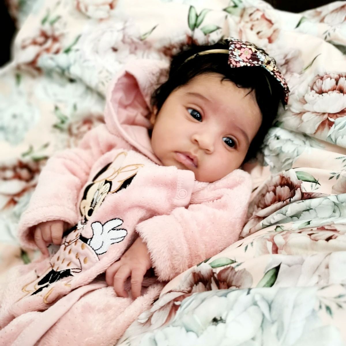 Baby in pink outfit resting on floral patterned bedding.