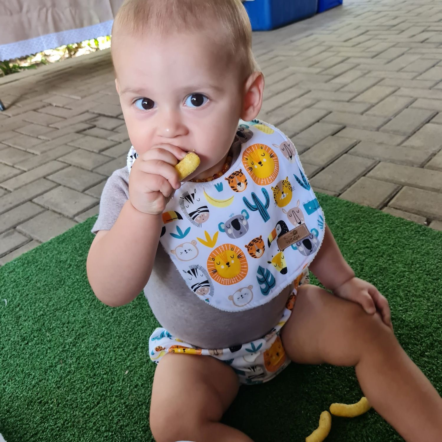 Baby in animal print bib crawls on artificial grass surface.