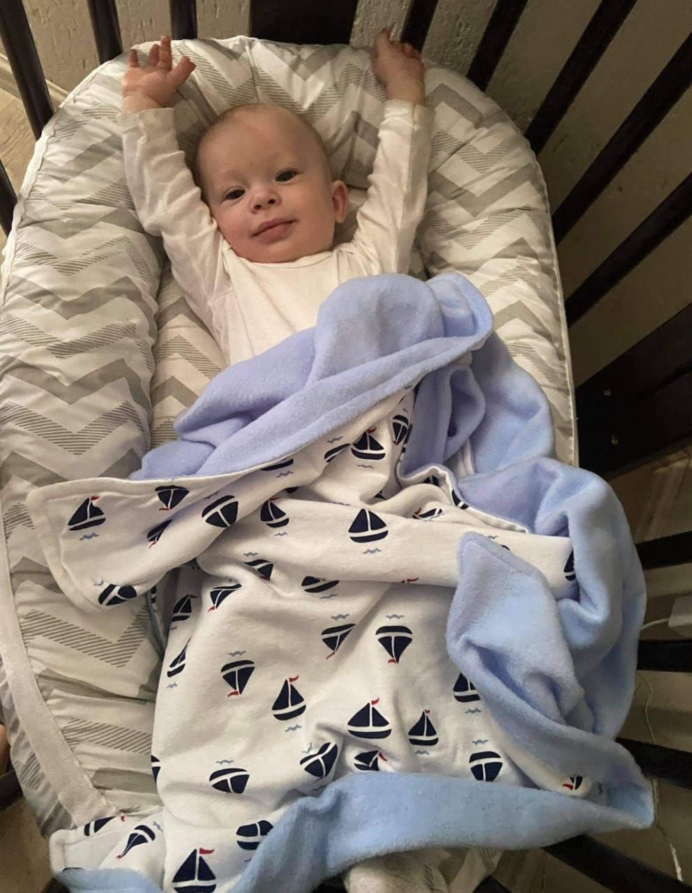 Baby in nautical-themed sleeper with sailboat pattern rests on chevron bedding.
