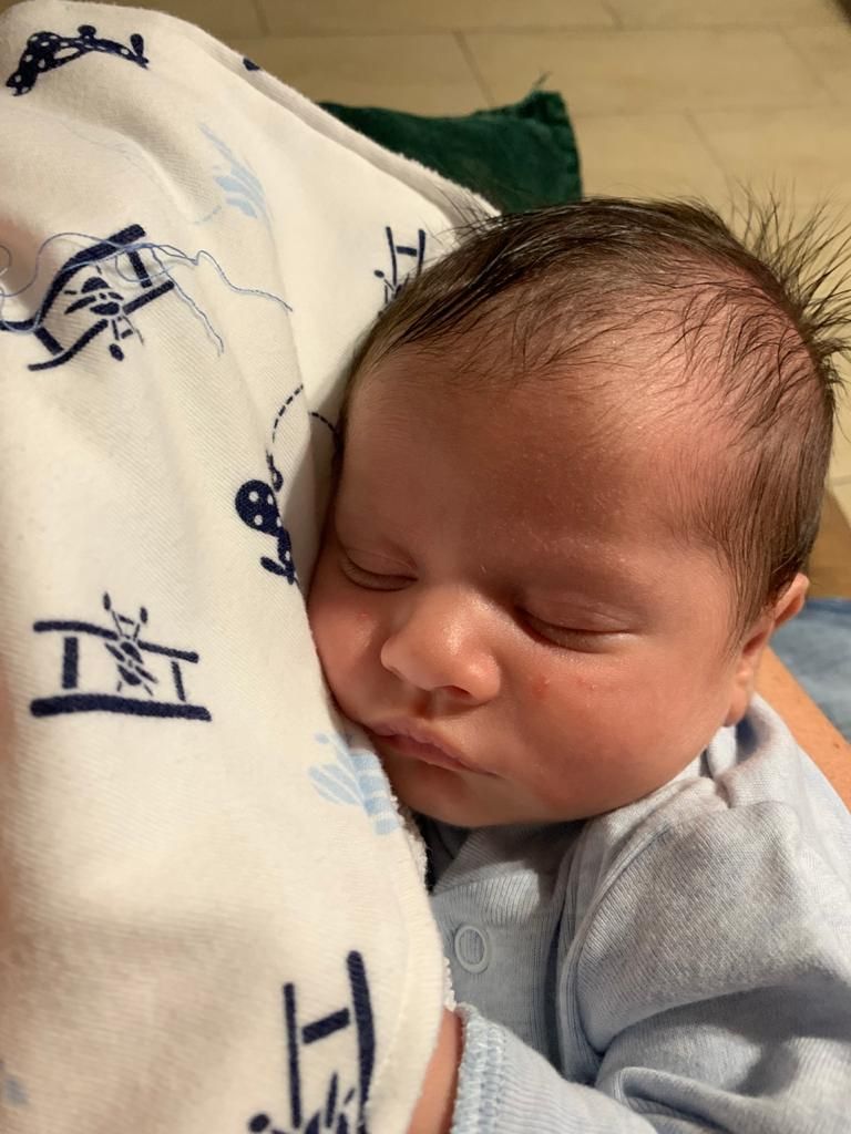 Sleeping newborn wearing light blue clothing rests on white patterned blanket.
