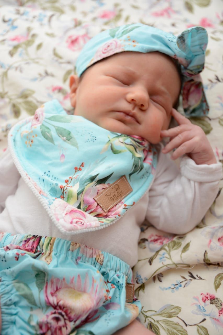 Baby wearing mint green floral bib sleeping on rose patterned fabric.