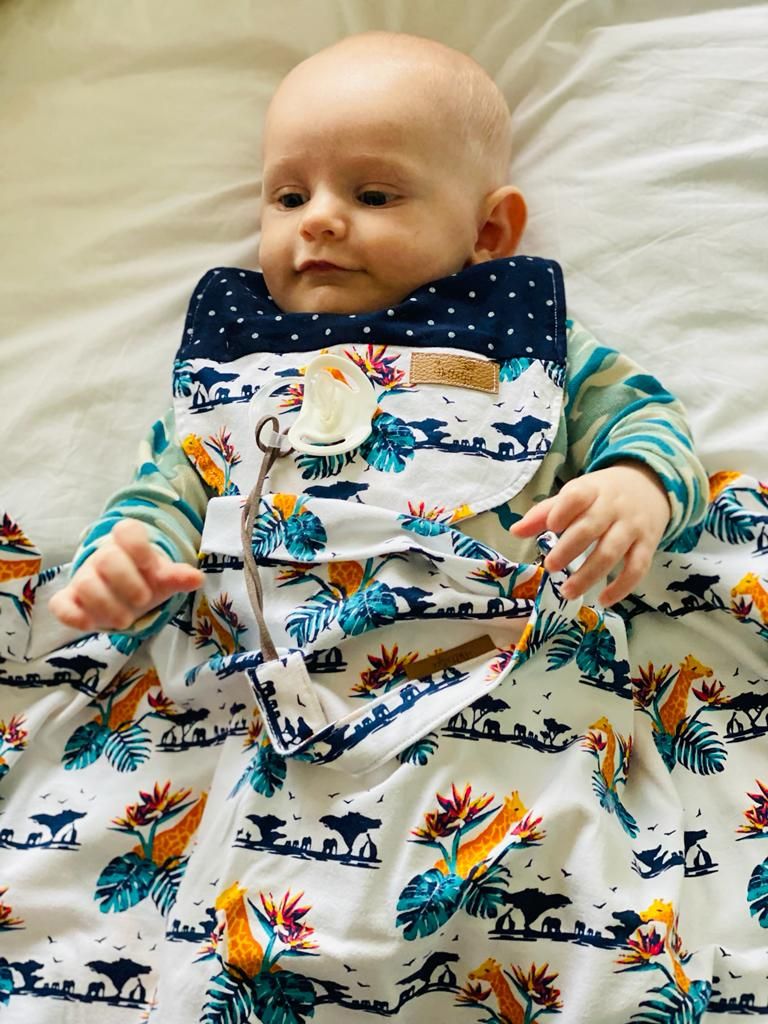 Baby wearing tropical print outfit lying on light colored bedding.