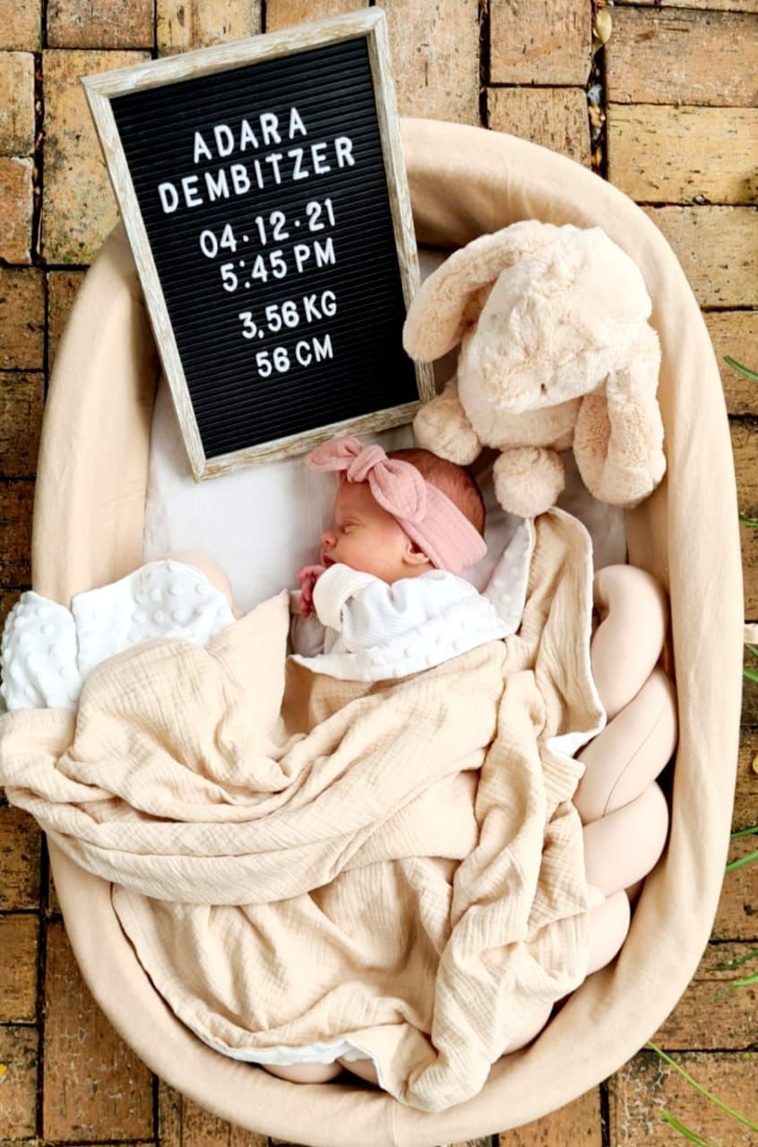 Newborn in bassinet with letter board displaying birth details and weight.