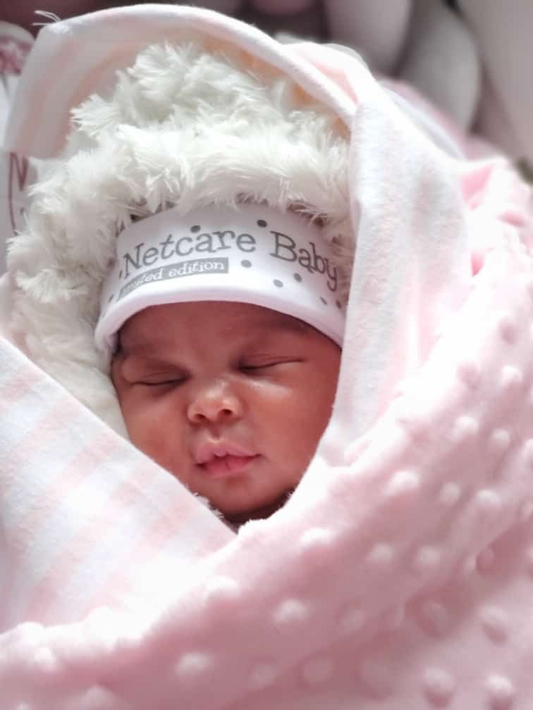 Newborn sleeping peacefully wrapped in soft pink blanket with hospital cap.