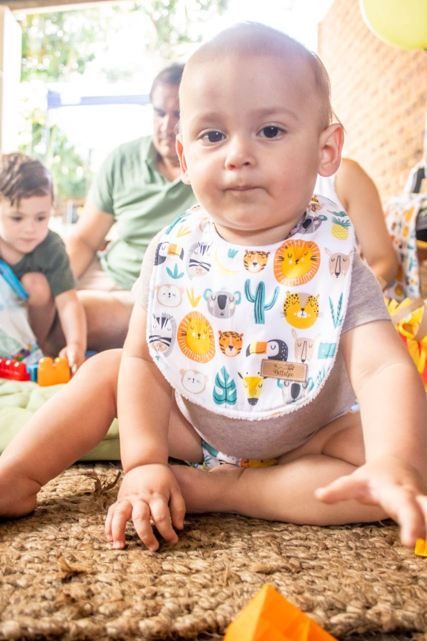 Baby wearing a cute animal print bib lies on a brown carpet while playing.