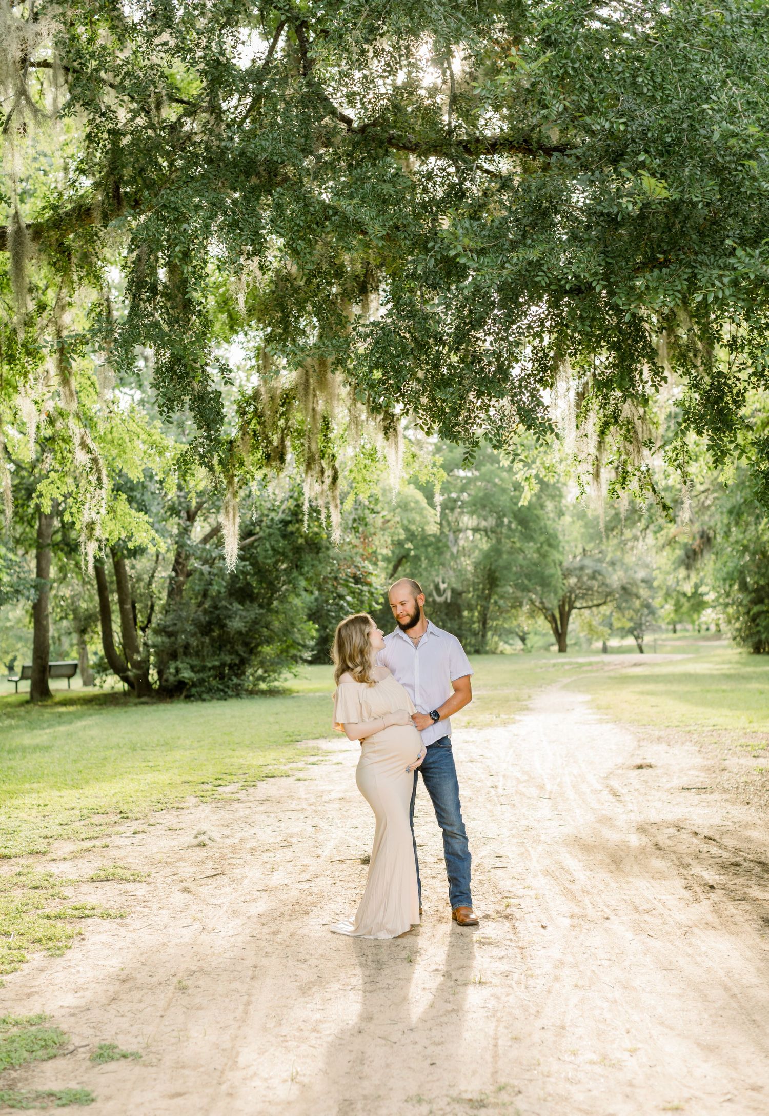 Romantic maternity photo under Spanish moss trees on sandy path.