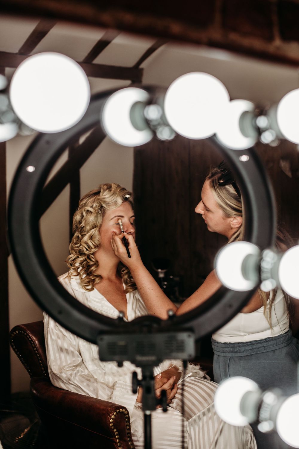 Wedding makeup application reflected in a round mirror with dramatic lighting.