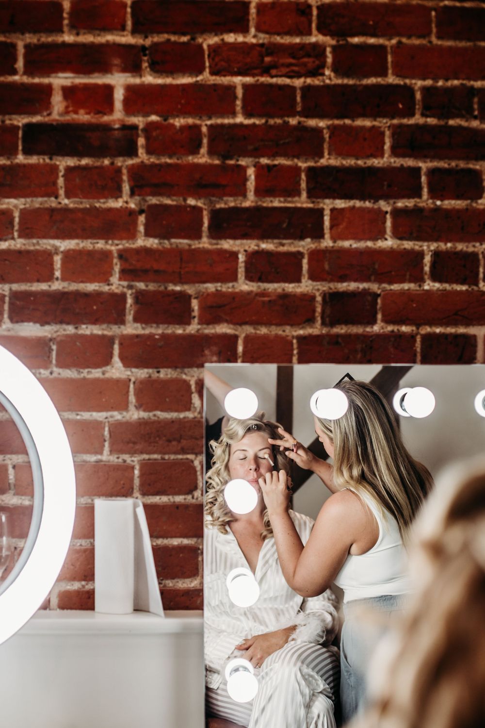 Wedding preparation scene against exposed brick wall with illuminated makeup mirror.