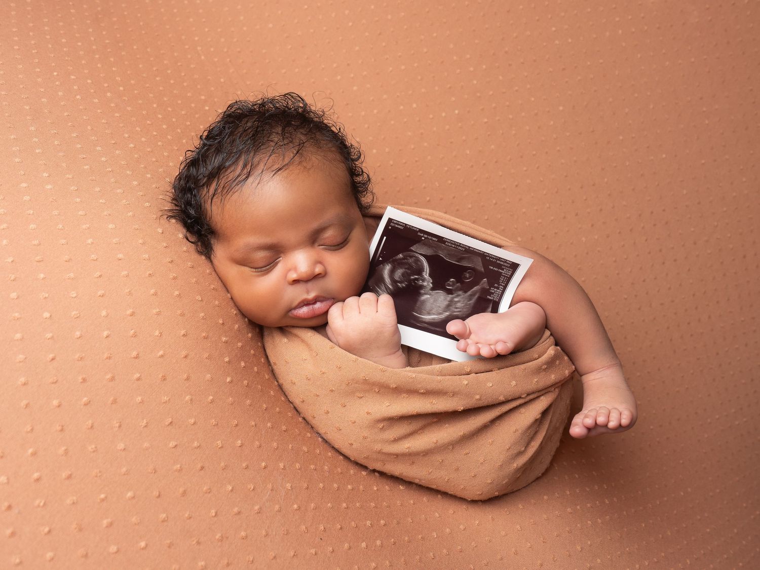 sleeping baby boy wrapped in a brown dotty blanket holding scan photo at newborn photoshoot in Doncaster.