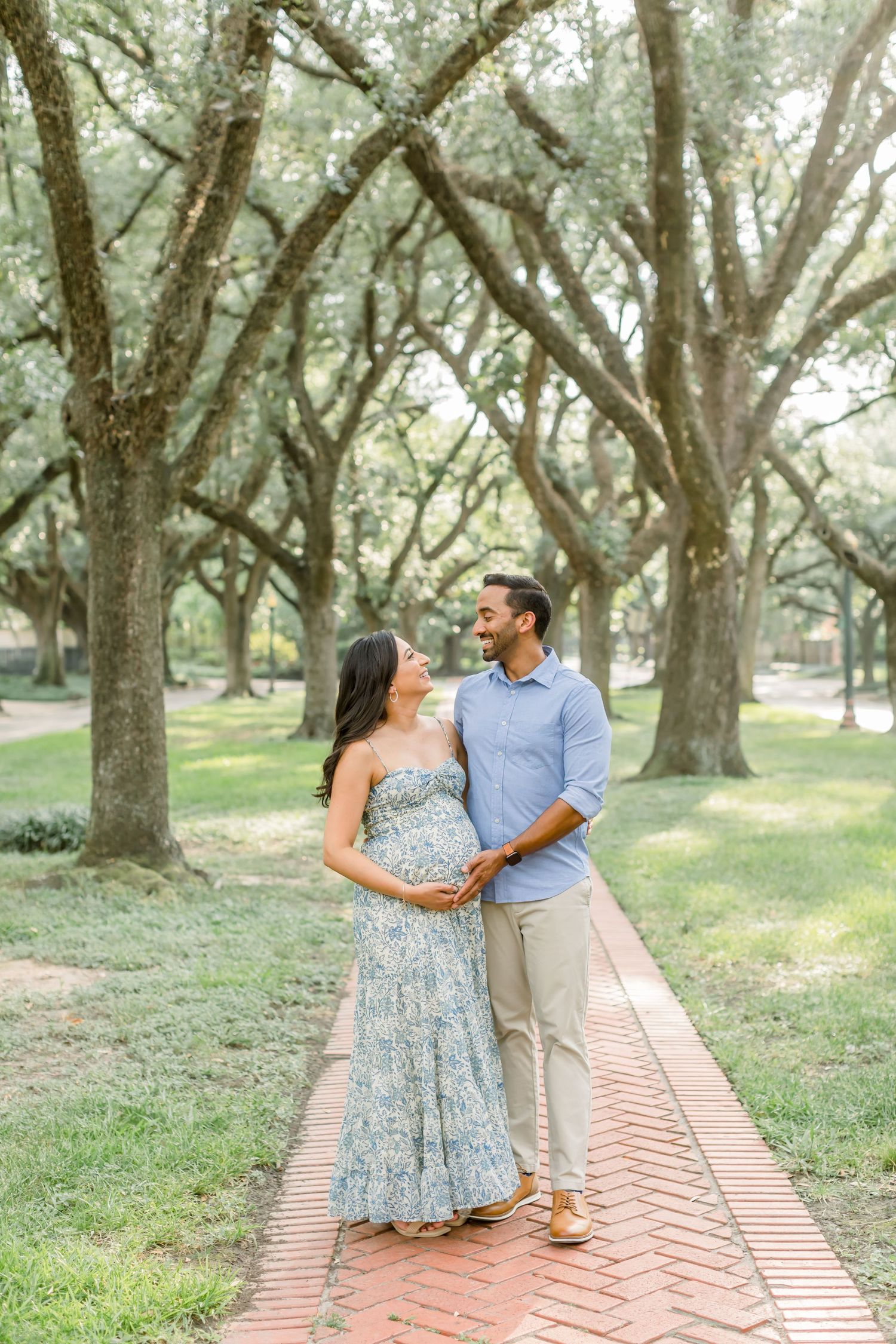 Maternity photoshoot on brick pathway surrounded by majestic oak trees.