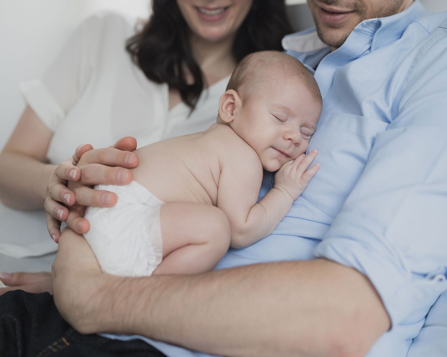 Sleeping newborn in diaper resting peacefully between parents on soft surface.