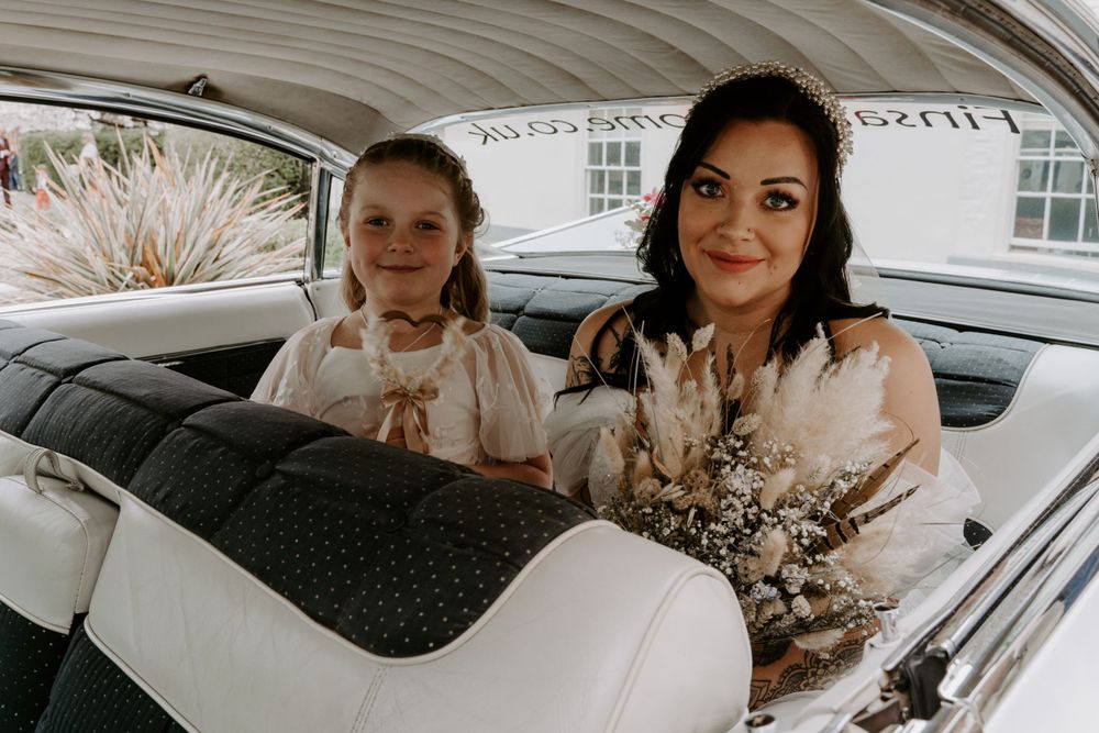a bride sitting in the back of a wedding car with her flower girl