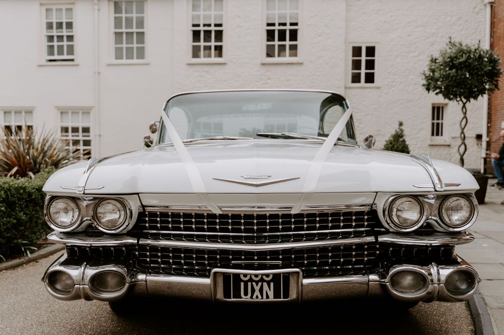 a white cadillac wedding car with a white ribbon on the front