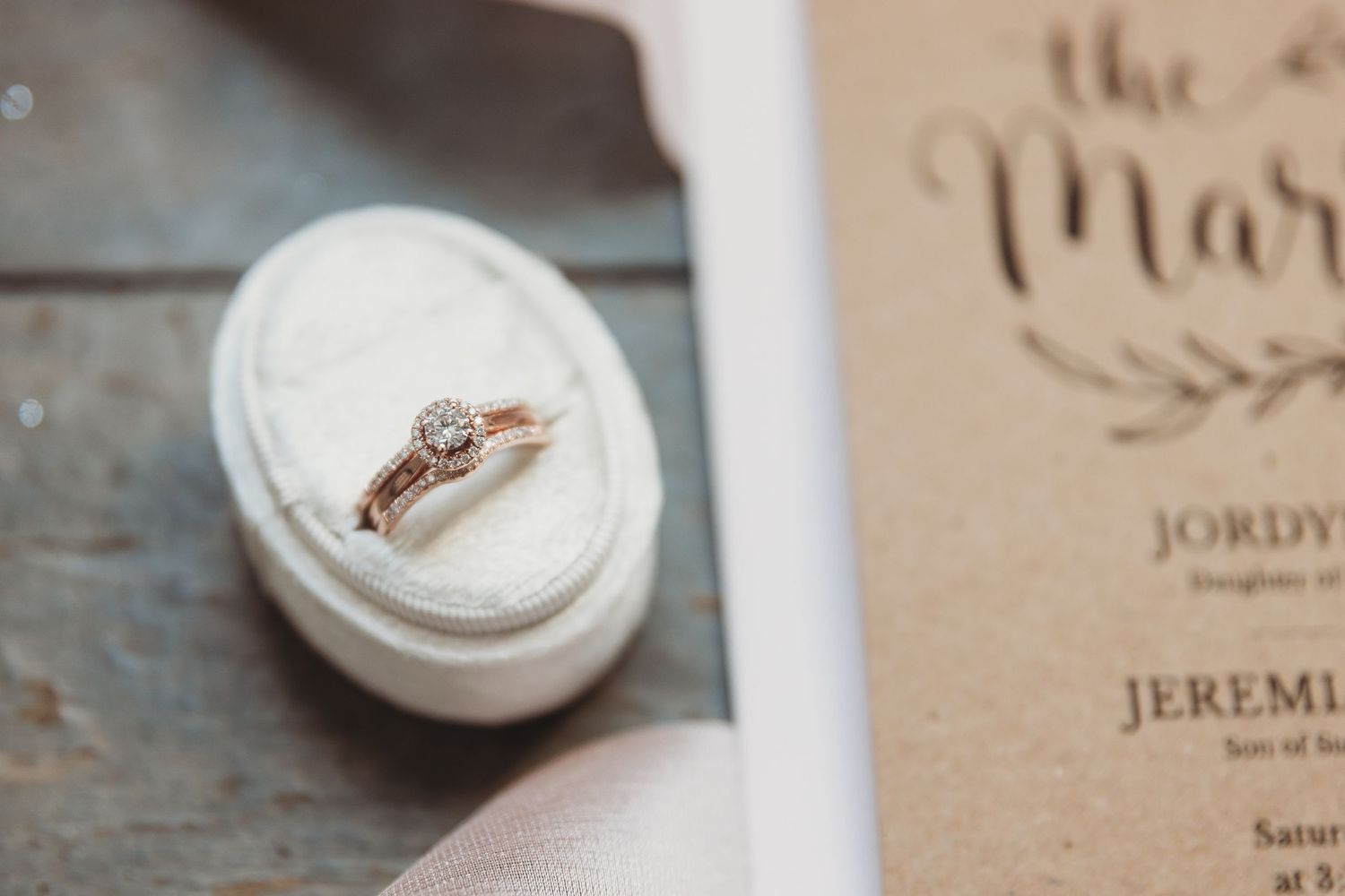 A delicate engagement ring rests in a white ring box on a rustic wooden surface.
