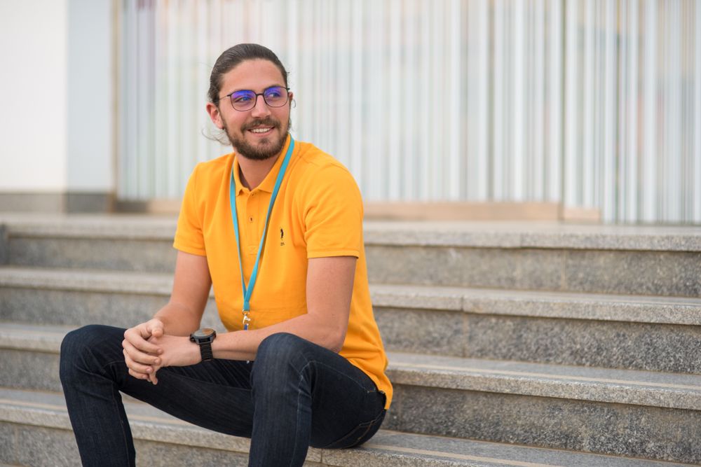 Person in yellow t-shirt and glasses sitting on concrete steps outdoors.