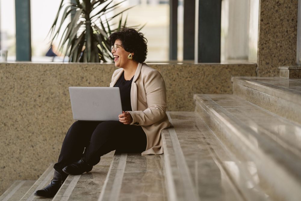 Professional working on laptop while sitting on concrete steps outdoors.