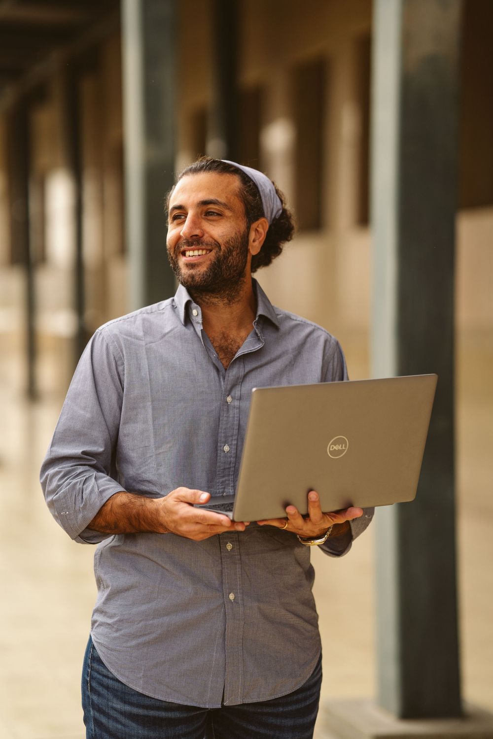 Professional in business casual attire working on laptop in outdoor office corridor.
