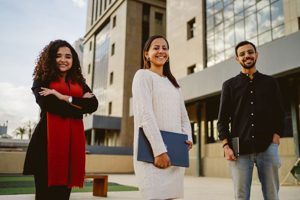 Three colleagues standing confidently outside modern office building.