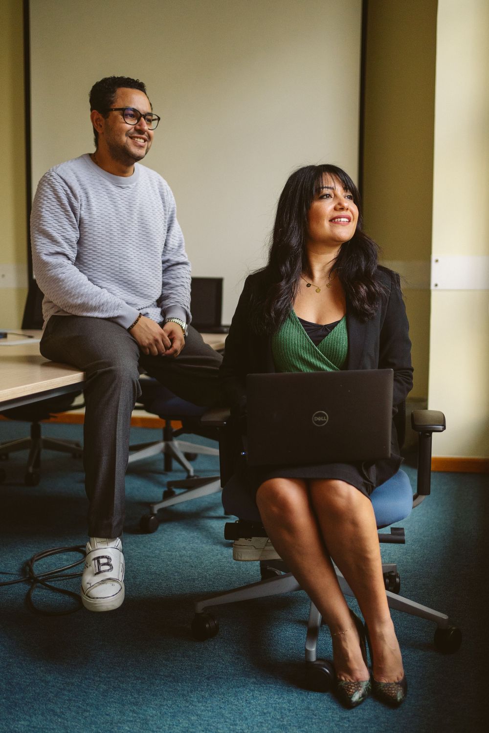 Two professionals having a casual meeting in an office space with a laptop and blue carpet.