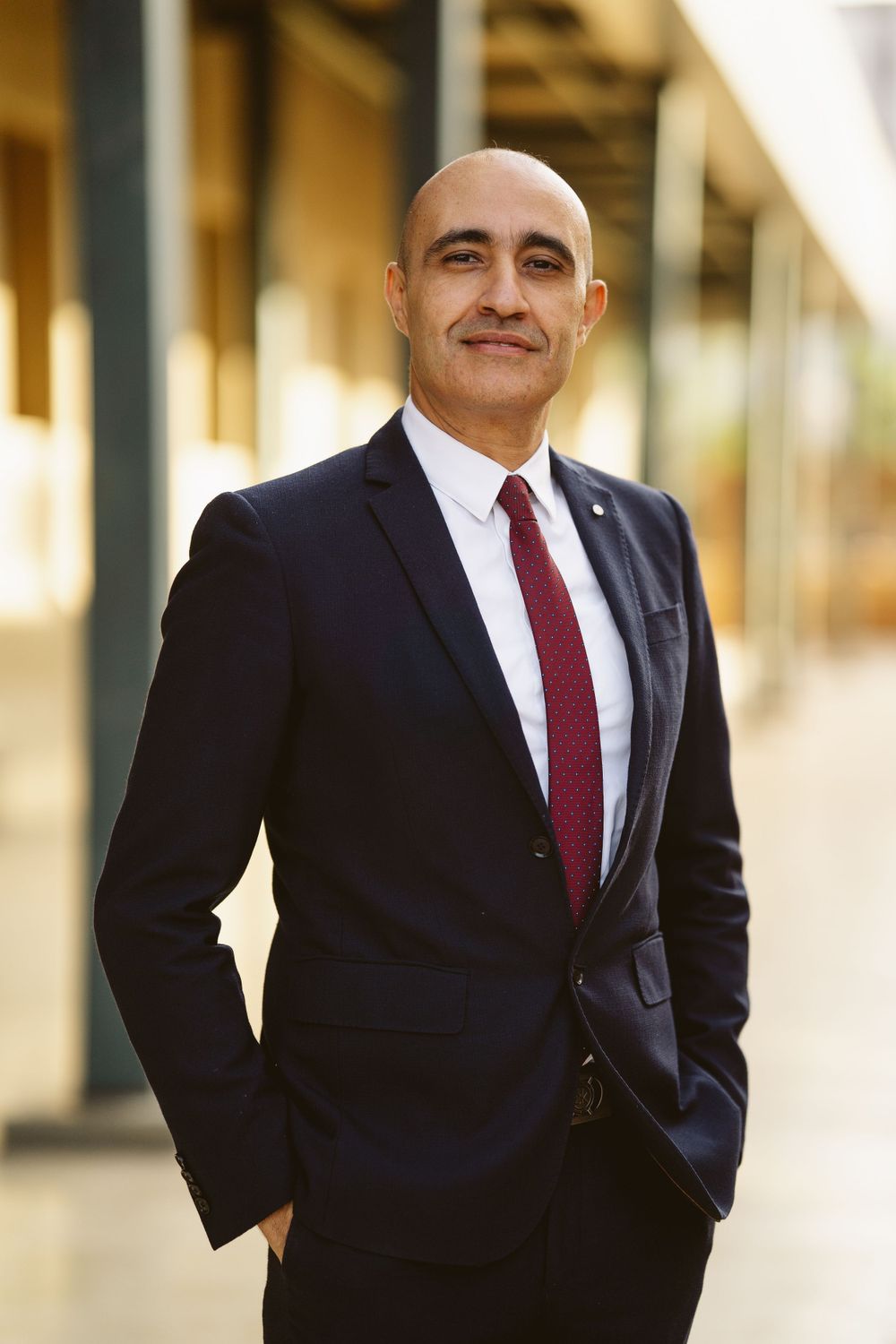 Professional in dark suit and red tie standing confidently with hands in pockets.