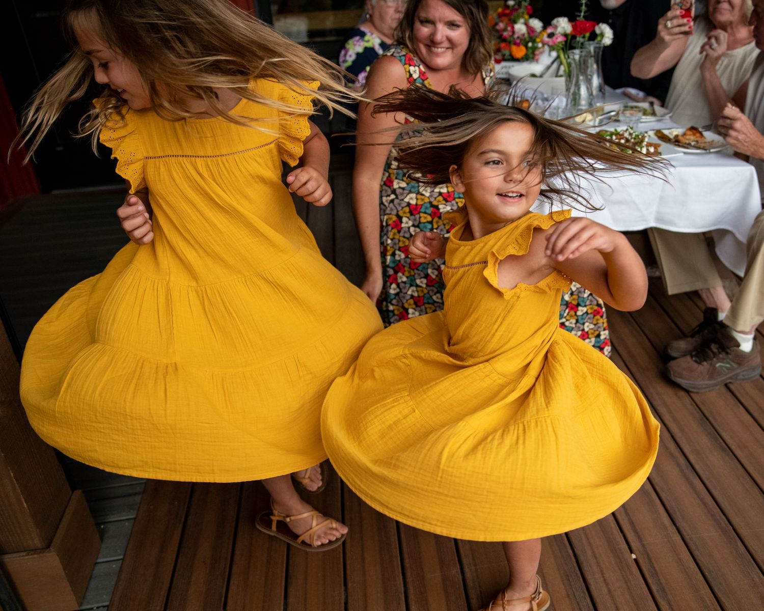 Two dancers in bright yellow dresses twirling at an indoor reception.