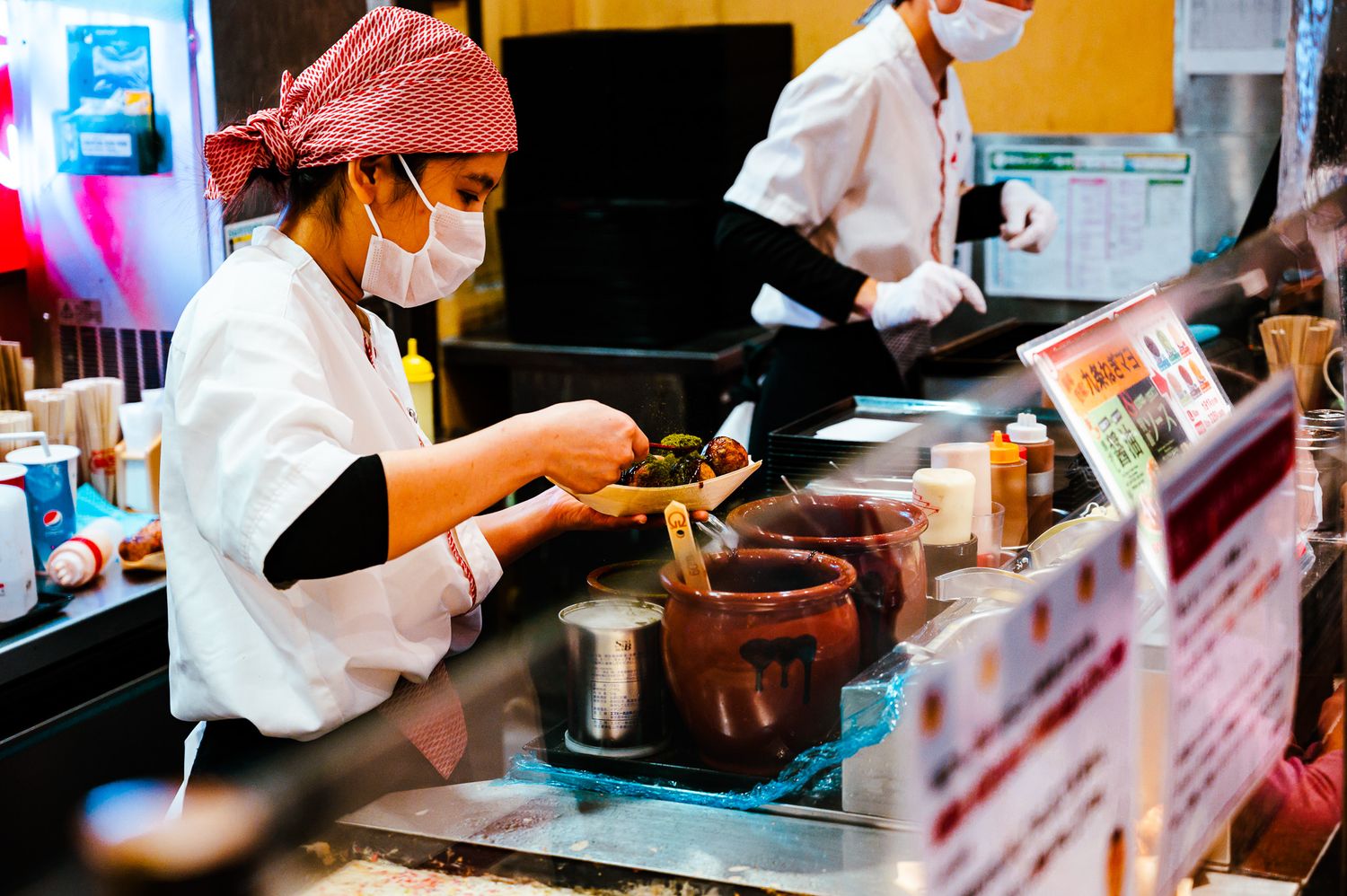 Chef preparing food at a Japanese restaurant counter with a red cap and white uniform.